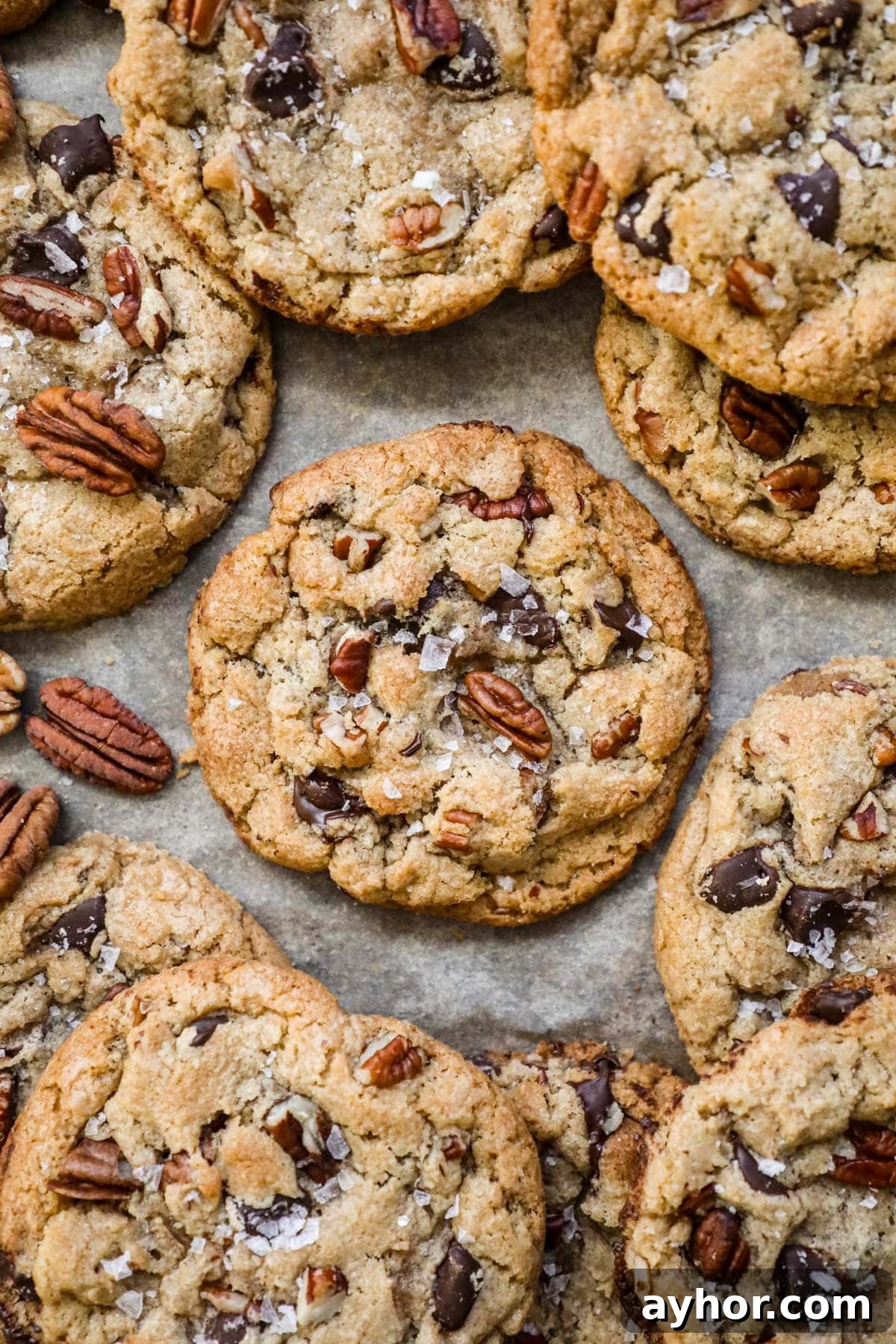 Warm and chewy browned butter pecan chocolate chip cookies with flaky sea salt on a parchment paper-lined baking sheet.
