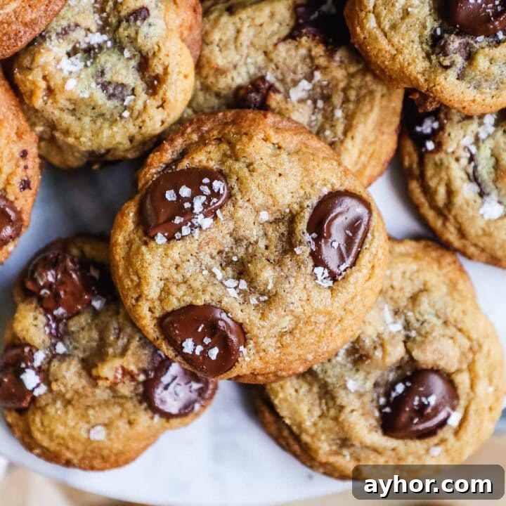 Crispy chewy chocolate chip walnut cookies stacked on a marble cake stand.