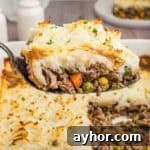 A close-up shot of a spoonful of cottage pie, highlighting the creamy mashed potato topping and hearty beef and vegetable filling, with the casserole dish in the background.