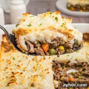 A close-up shot of a spoonful of cottage pie, highlighting the creamy mashed potato topping and hearty beef and vegetable filling, with the casserole dish in the background.