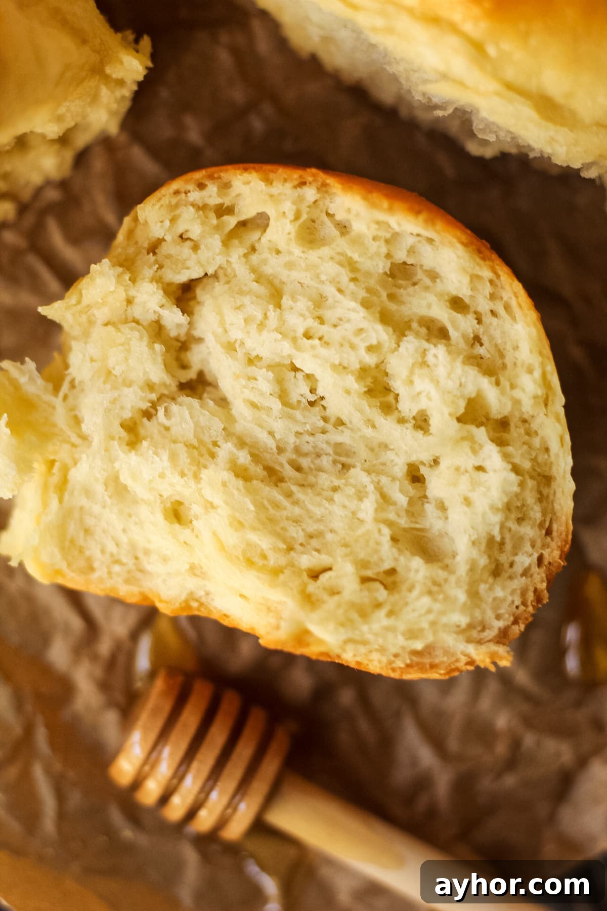 1-Hour Soft and Fluffy Dinner Rolls Recipe 12 honey butter dinner rolls on parchment paper. One roll torn open to show texture.