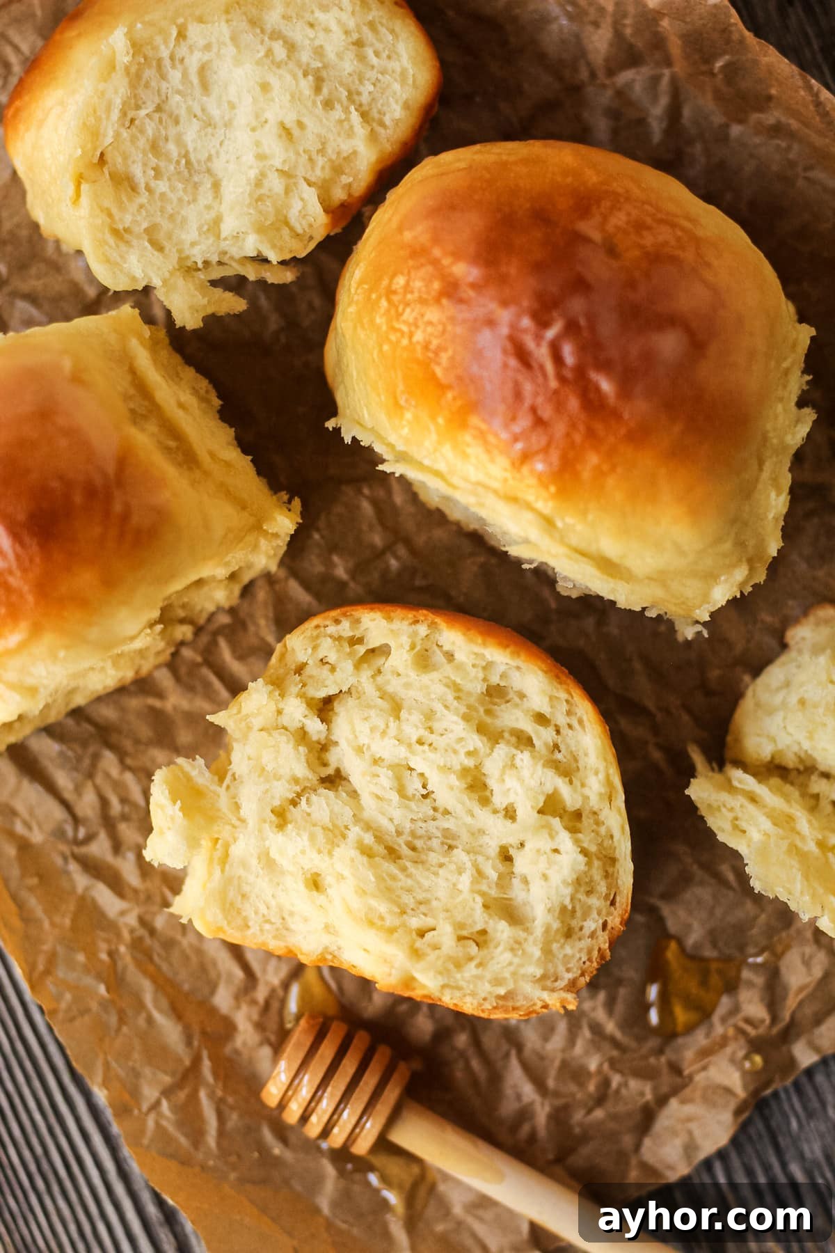 1-Hour Soft and Fluffy Dinner Rolls Recipe 4 honey butter dinner rolls on parchment paper. One roll torn open to show texture.