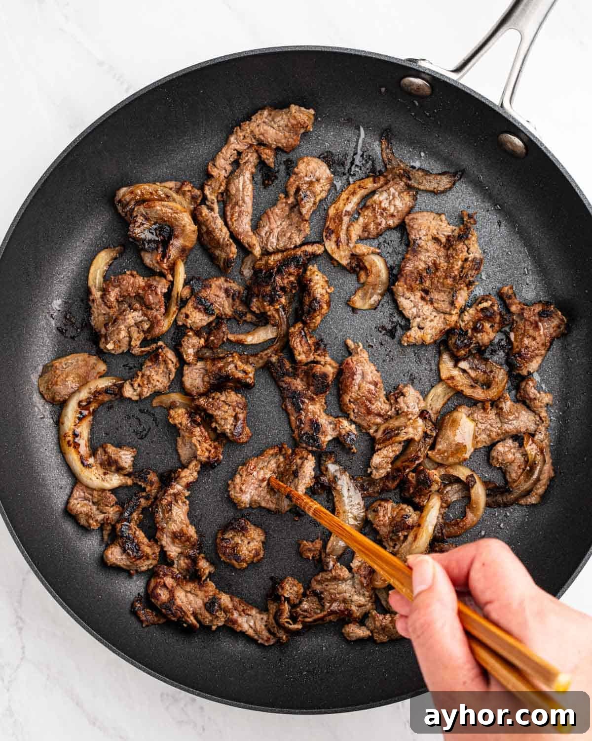 Bulgogi in a pan with chopsticks flipping a piece of beef.