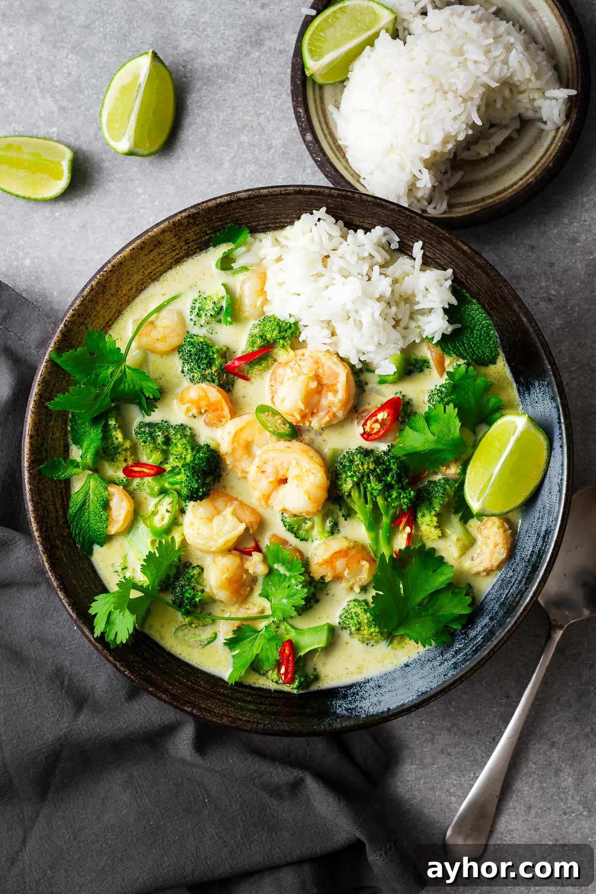 A five-ingredient Thai green curry with prawn tails and a side of rice, garnished with lime wedges and fresh herbs.