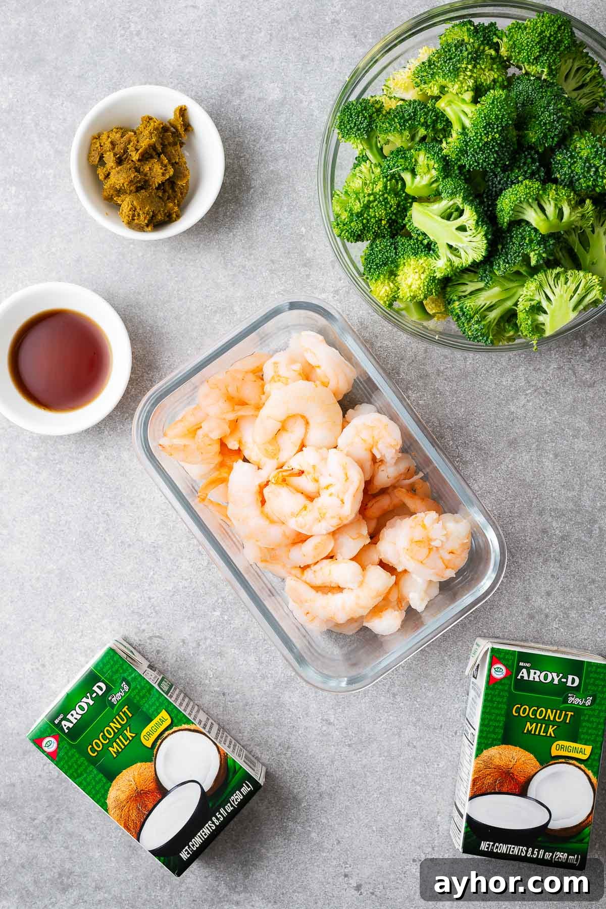 The five main ingredients for Thai green curry including green curry paste, coconut milk, fish sauce, vegetables and a protein with prawn tails pictured.