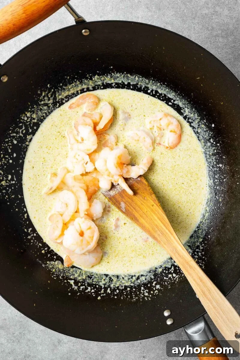 Shrimp added to a wok with green curry sauce.