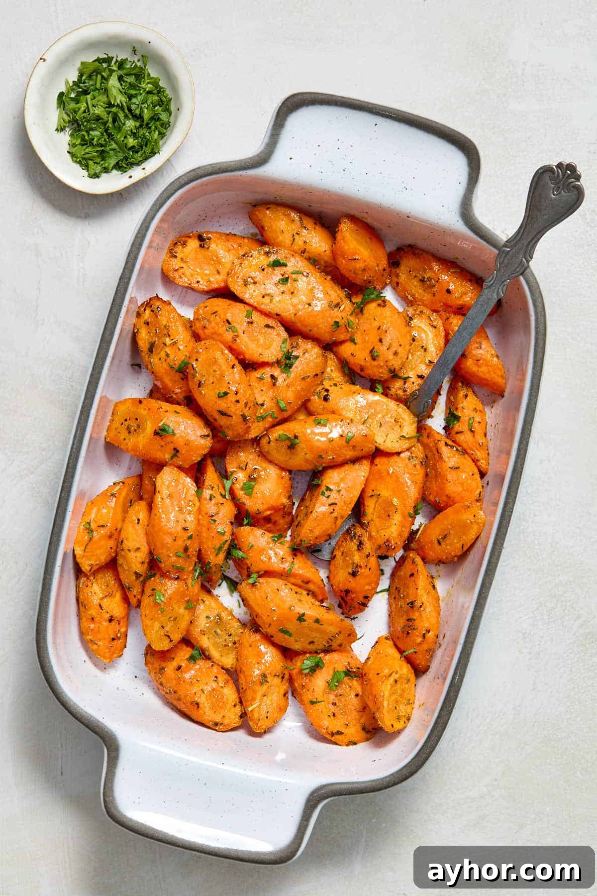 Carrots served in white dish with a spoon and chopped parsley on the side.