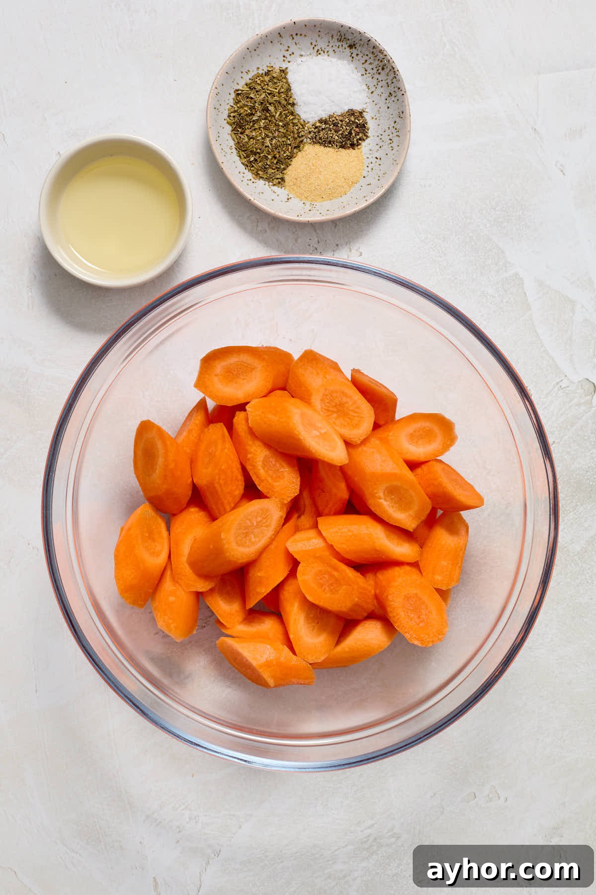 Sliced carrots in glass bowl with oil and seasonings on the side.
