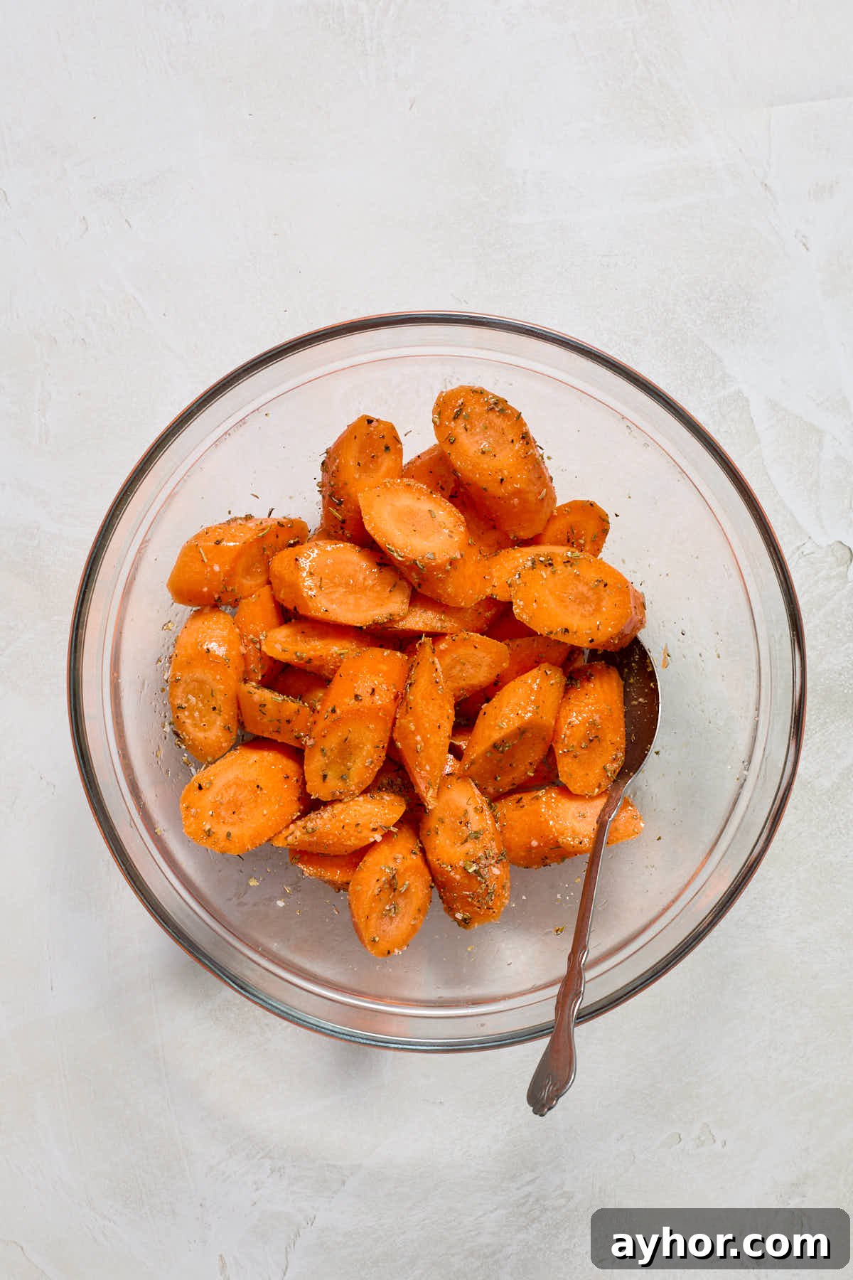 Sliced carrots in glass bowl tossed with oil and seasonings.