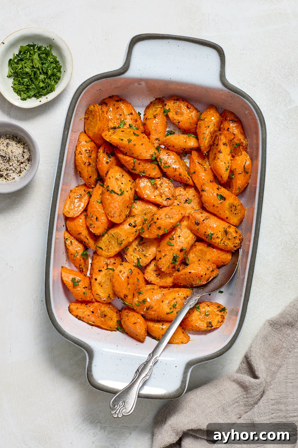 Carrots served in dish with herbs and salt and pepper in bowls on the side.
