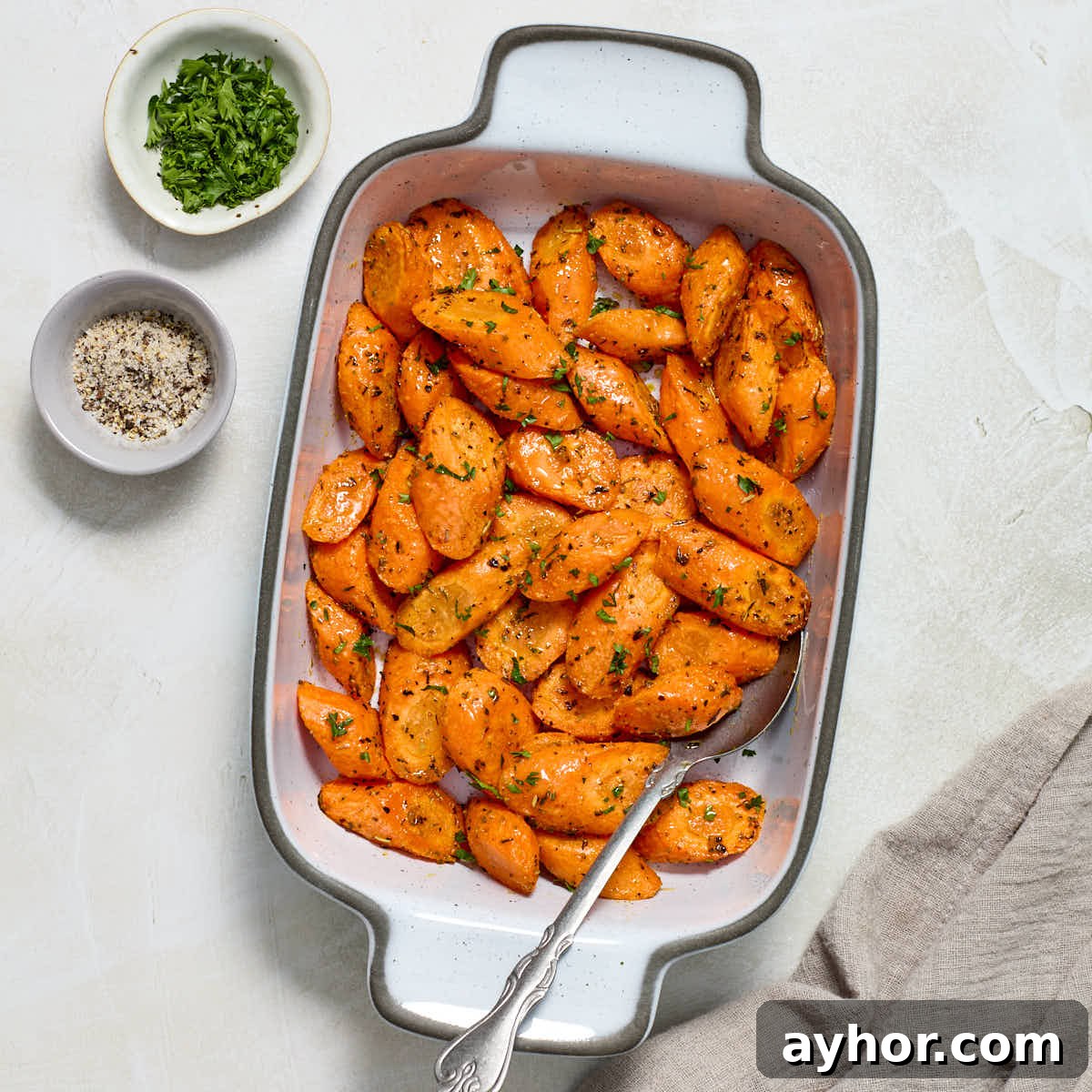 Air fryer carrots served in a white dish with fresh parsley and salt and pepper on the side.