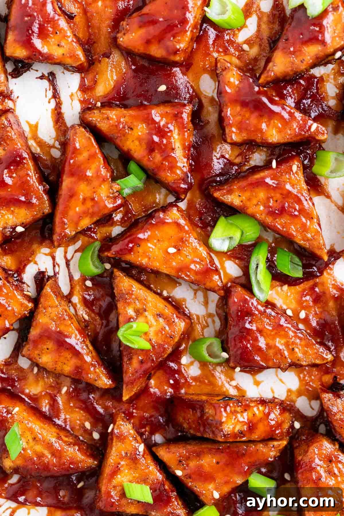 Grilled BBQ Tofu Recipe: Smoky, Glazed Plant-Based Dish 2 BBQ tofu triangles topped with green onions and sesame seeds on a white background