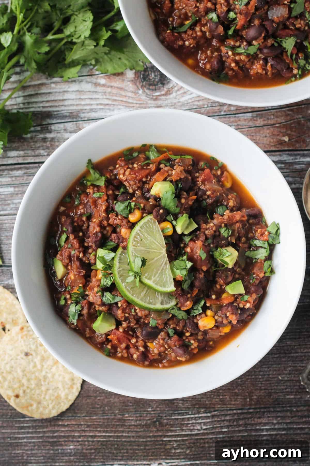 Bowl of black bean quinoa chili topped with diced avocado and two lime slices.