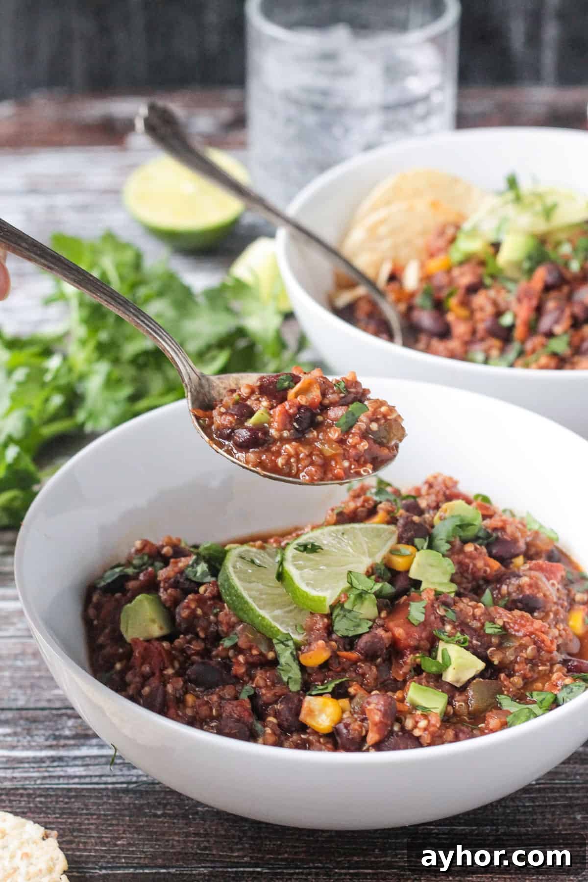 Spoonful of chili with black beans and quinoa being lifted out of a white bowl. 