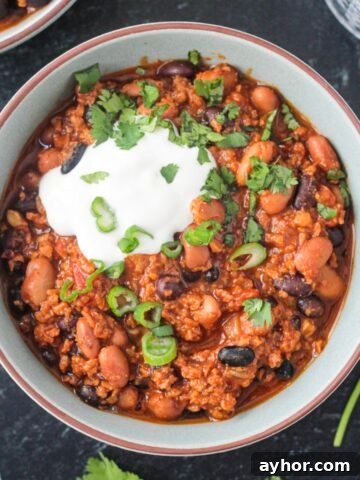 Vegan chorizo chili in a bowl with a dollop of sour cream and green onions.