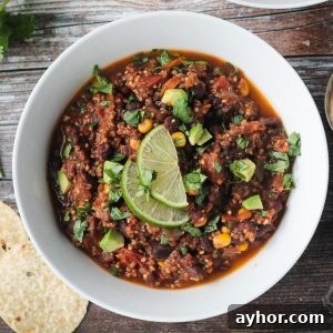 Bowl of black bean quinoa chili topped with diced avocado and two lime slices.