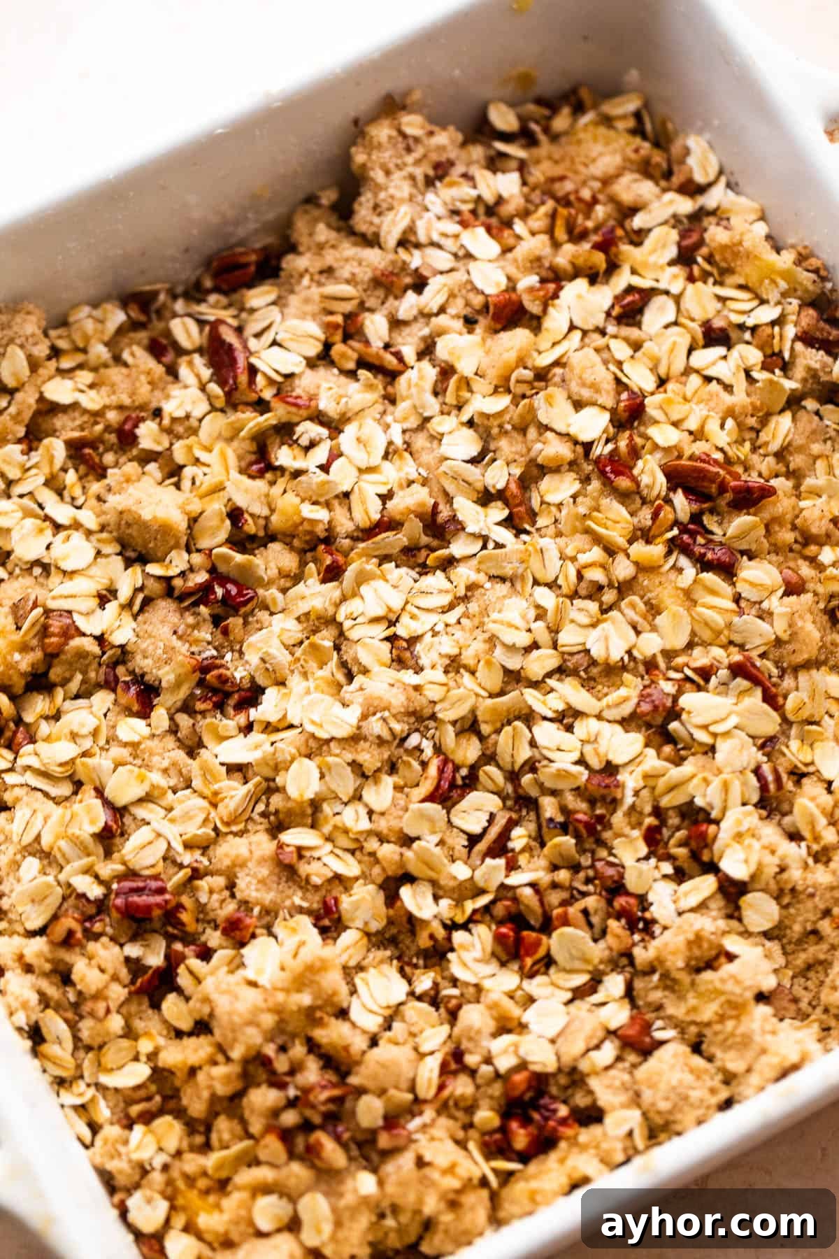 Perfect Peach Crisp Recipe for Summer Baking 5 squared baking dish with peach slices covered in oats, flour, and pecans