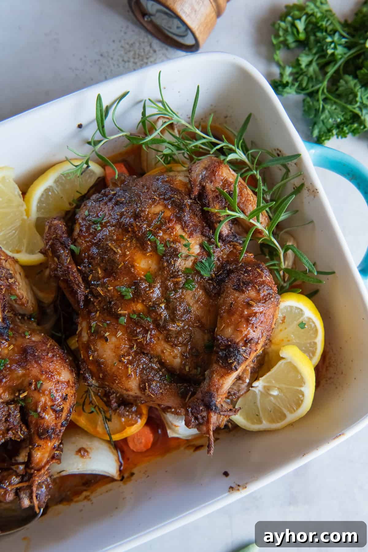 Crispy Roasted Cornish Game Hens with Garlic and Herbs 6 A close up of cornish games hens in a baking dish with vegetables, lemon, and sprigs of fresh rosemary.