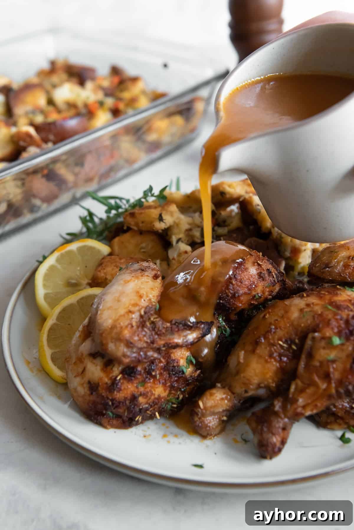 Crispy Roasted Cornish Game Hens with Garlic and Herbs 7 Gravy pouring from a gravy boat over cornish hens on a white plate.