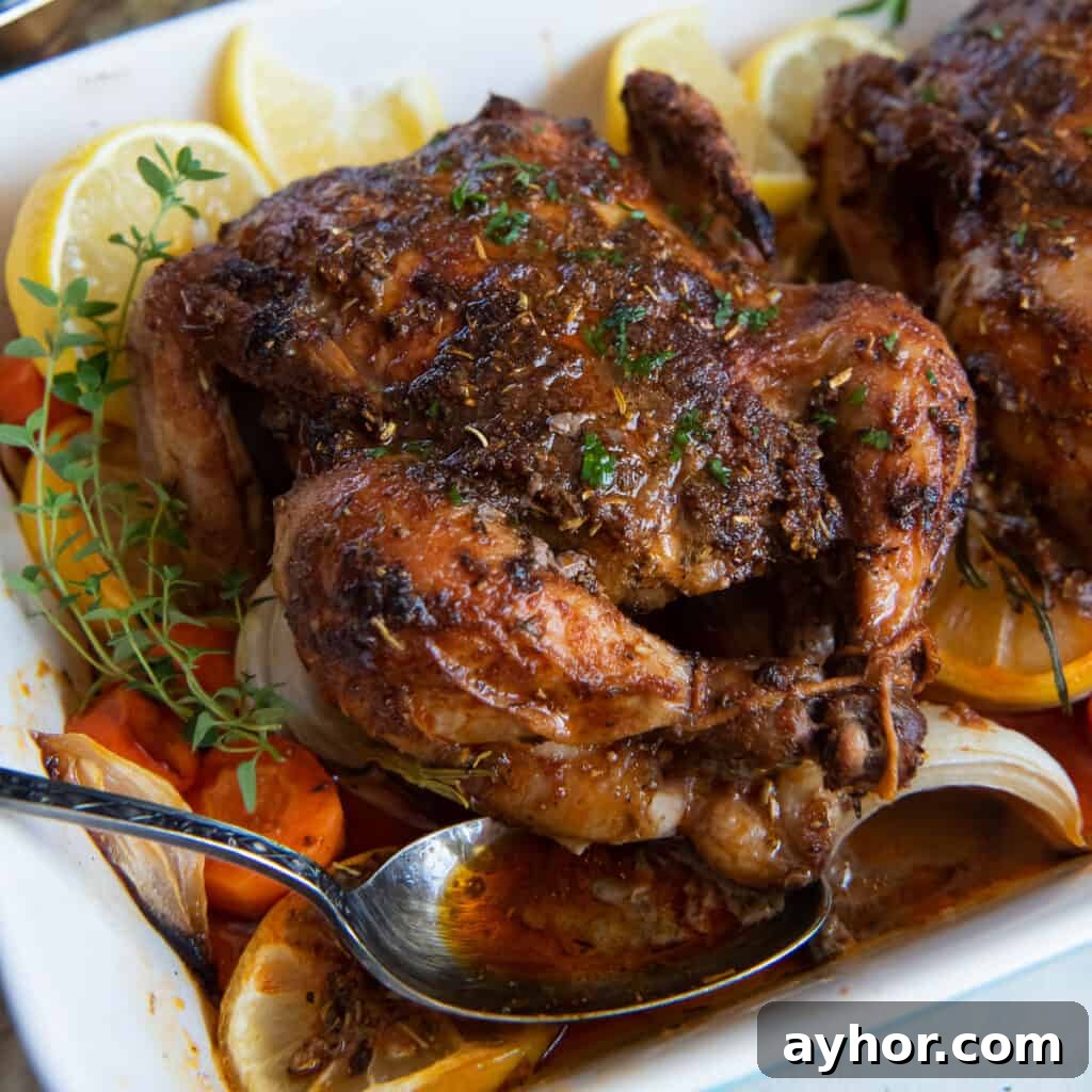 Crispy Roasted Cornish Game Hens with Garlic and Herbs 10 A spoon resting in a baking dish with roasted Cornish game hens on a bed of carrots, onions, and lemon slices.