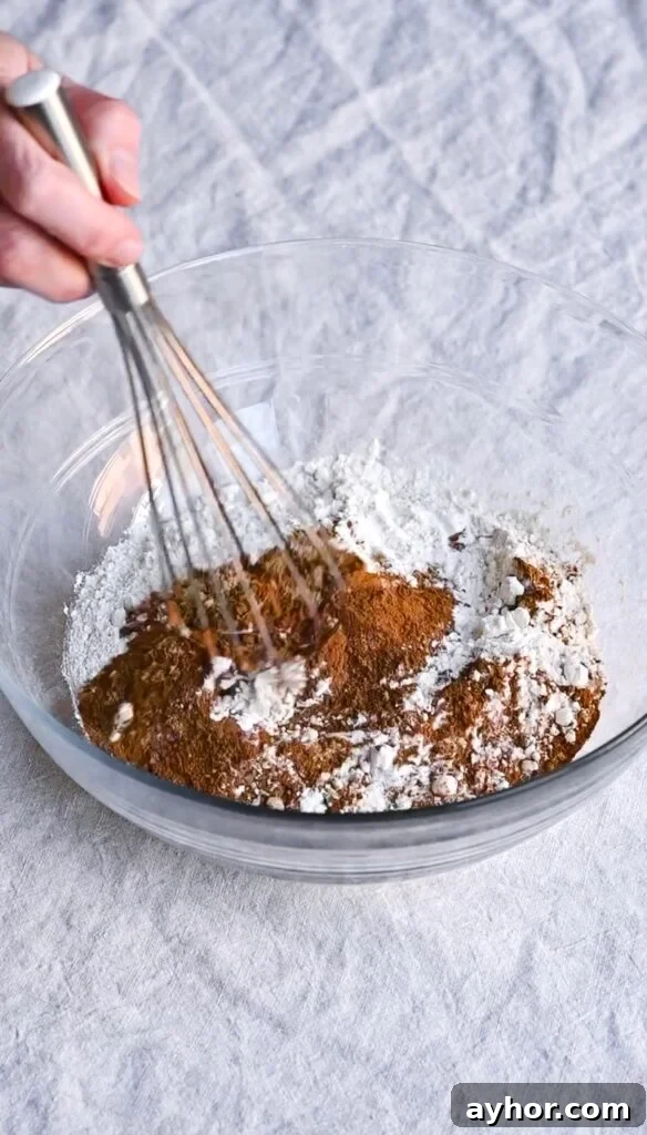 Moist Carrot Cake with Cream Cheese Frosting Recipe 3 Hand whisking flour and spices together in a large glass mixing bowl.