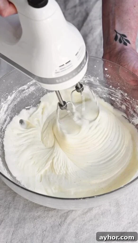 Moist Carrot Cake with Cream Cheese Frosting Recipe 9 Cream cheese cake frosting being whipped by an electric hand mixer in a bowl.