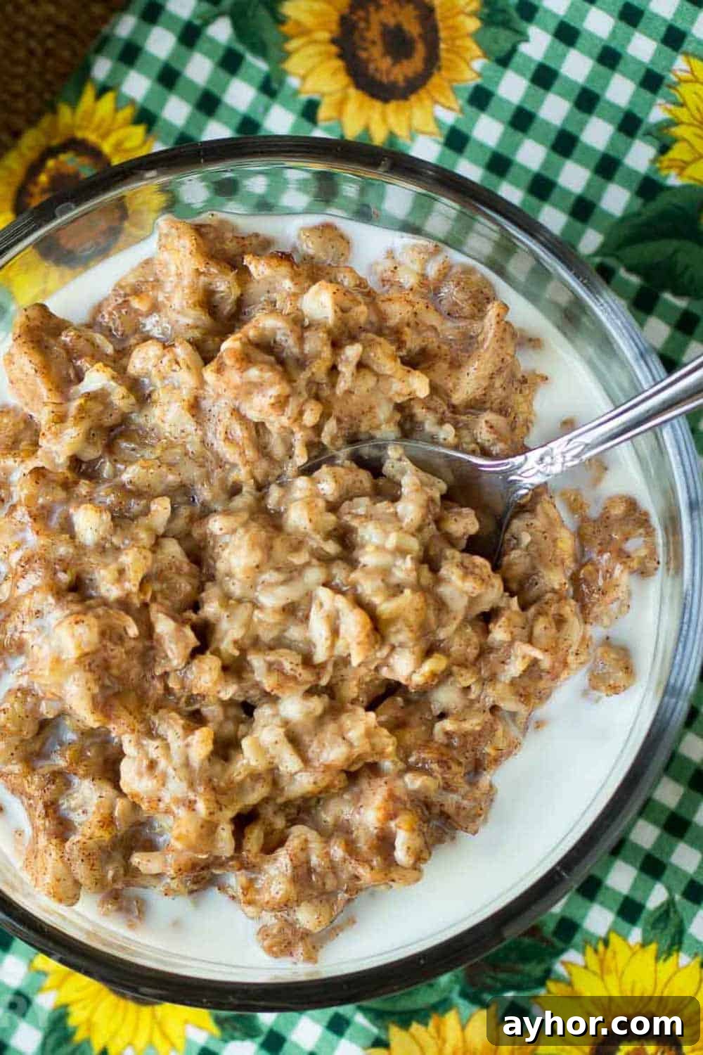 Maple Cinnamon Steel-Cut Oatmeal Made in a Slow Cooker 2 Overhead shot of oatmeal in a clear bowl with a spoon on a green checkered cloth with sunflowers.
