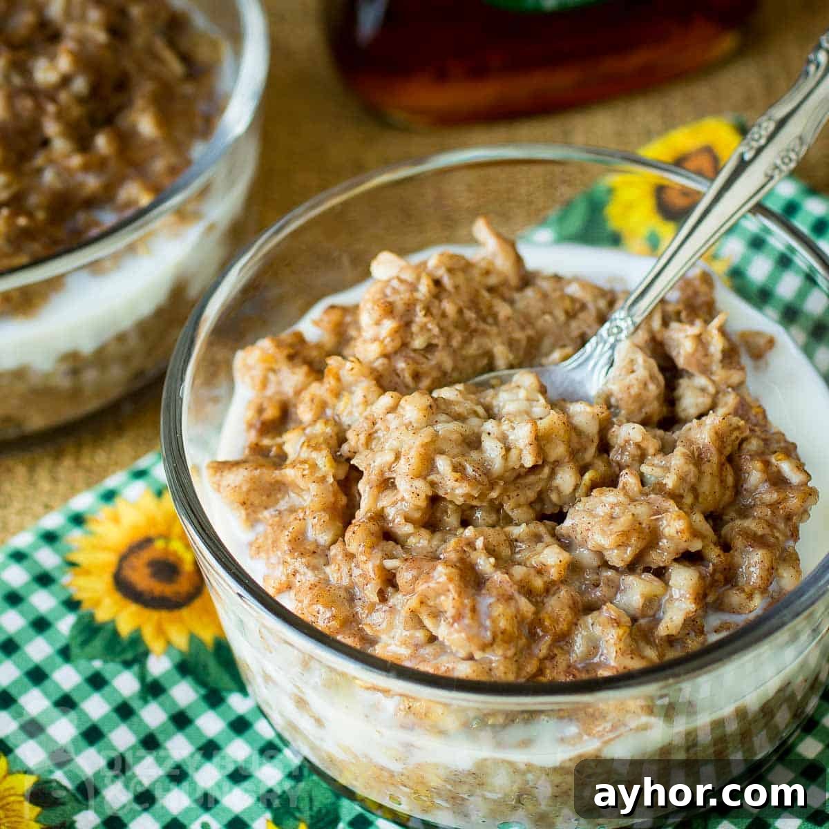 Maple Cinnamon Steel-Cut Oatmeal Made in a Slow Cooker 5 Side angled shot of oatmeal in a clear bowl with a spoon on a green checkered cloth with sunflowers.