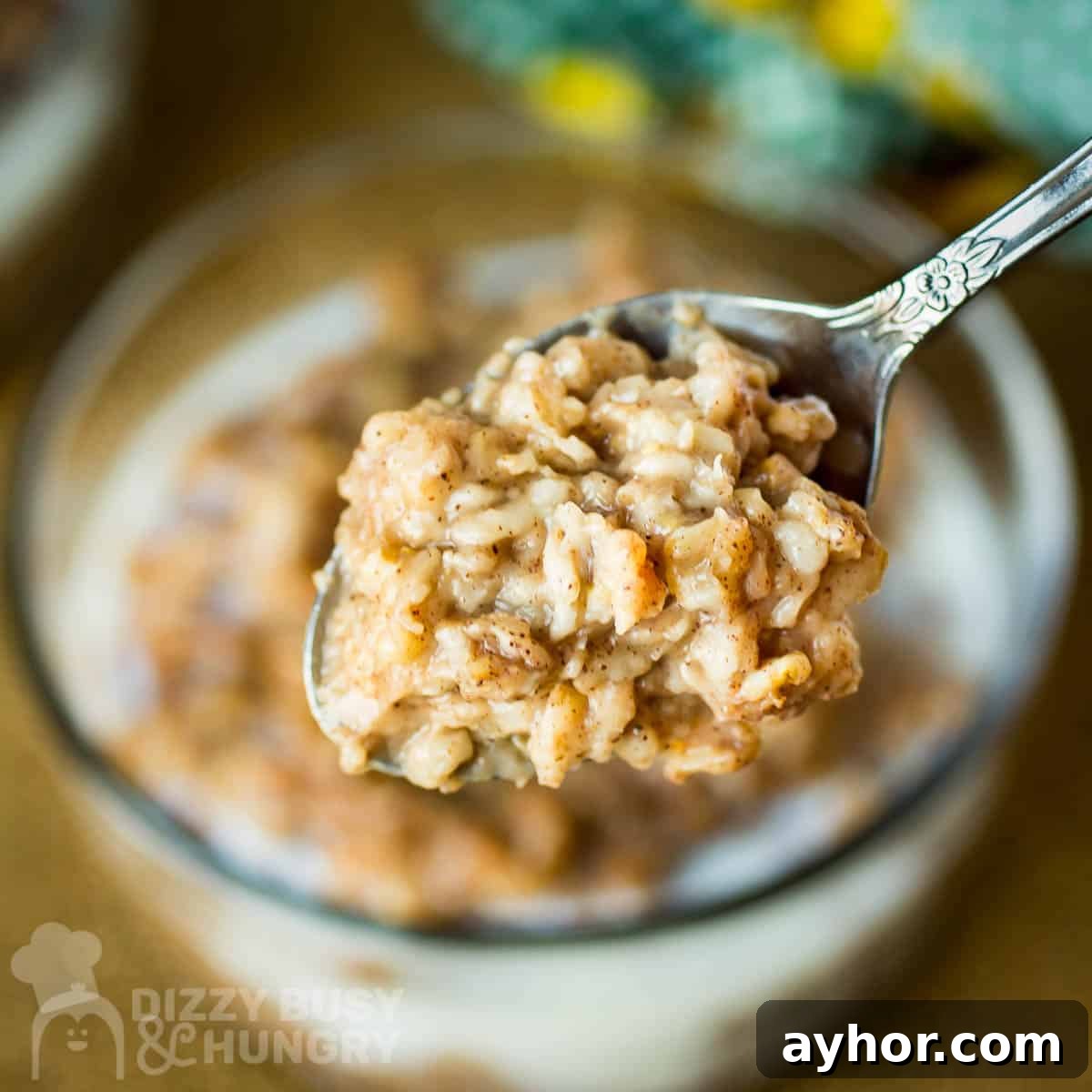 Maple Cinnamon Steel-Cut Oatmeal Made in a Slow Cooker 6 Close up shot of a spoon holding a bite of oatmeal over a clear bowl of oatmeal on a wooden surface.