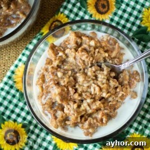 Maple Cinnamon Steel-Cut Oatmeal Made in a Slow Cooker 7 Overhead shot of oatmeal in a clear bowl with a spoon on a green checkered cloth with sunflowers.