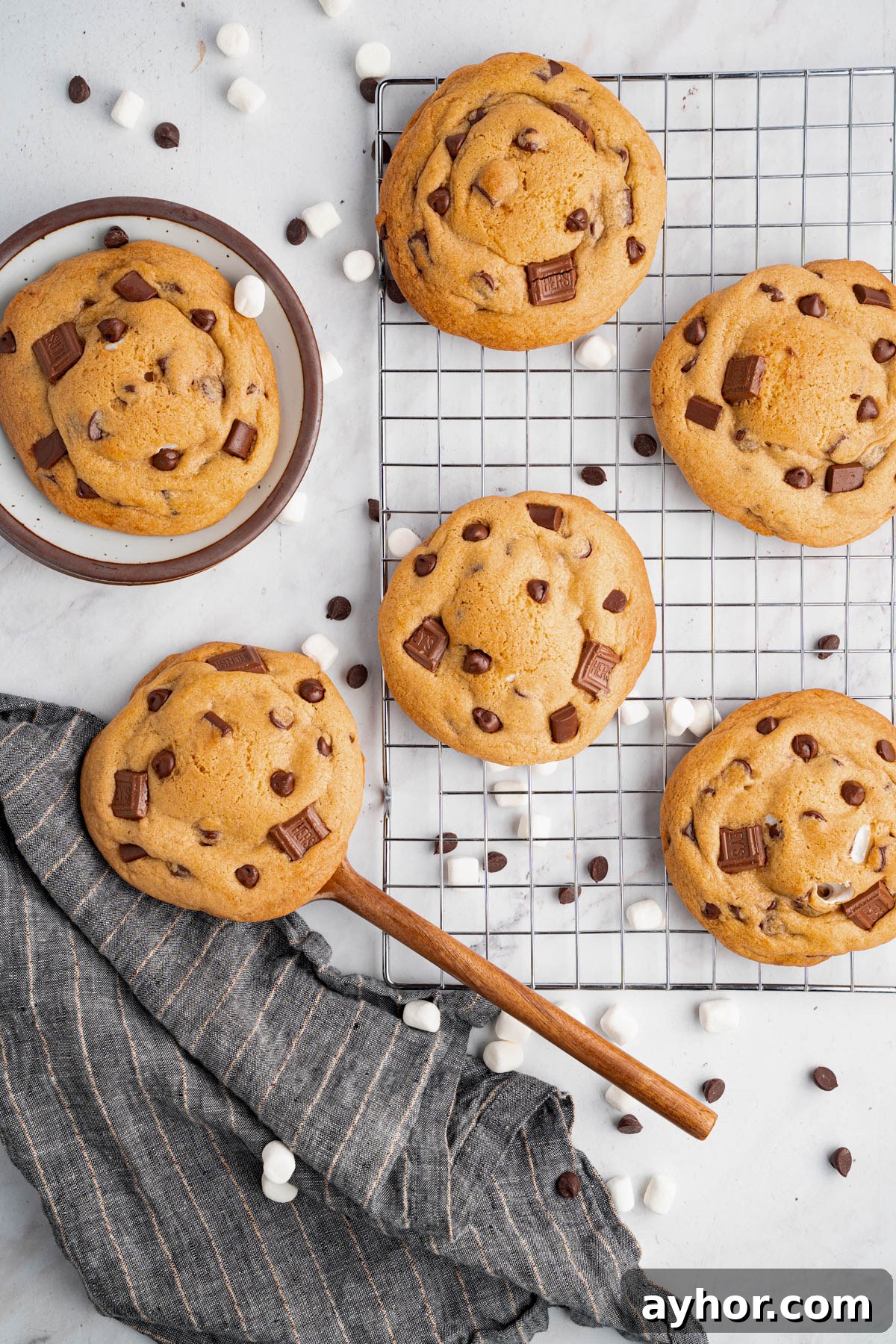 Ultimate S'mores Cookie Recipe: Crispy Edges & Gooey Centers 6 Six baked s’mores cookies sit on a baking rack after coming out of the oven. A spatula is scooping one of the cookies.