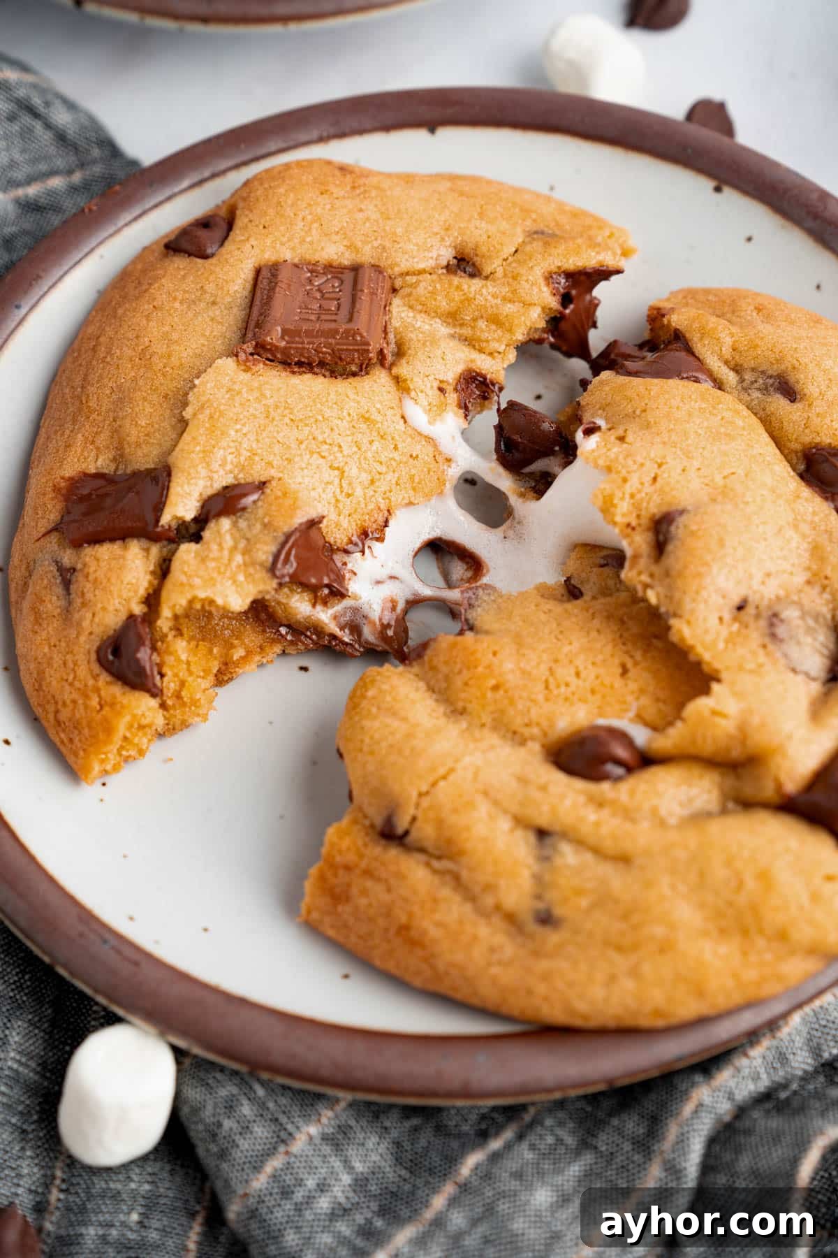 Ultimate S'mores Cookie Recipe: Crispy Edges & Gooey Centers 7 A s’mores cookie that is broken in half sits on a plate for serving.