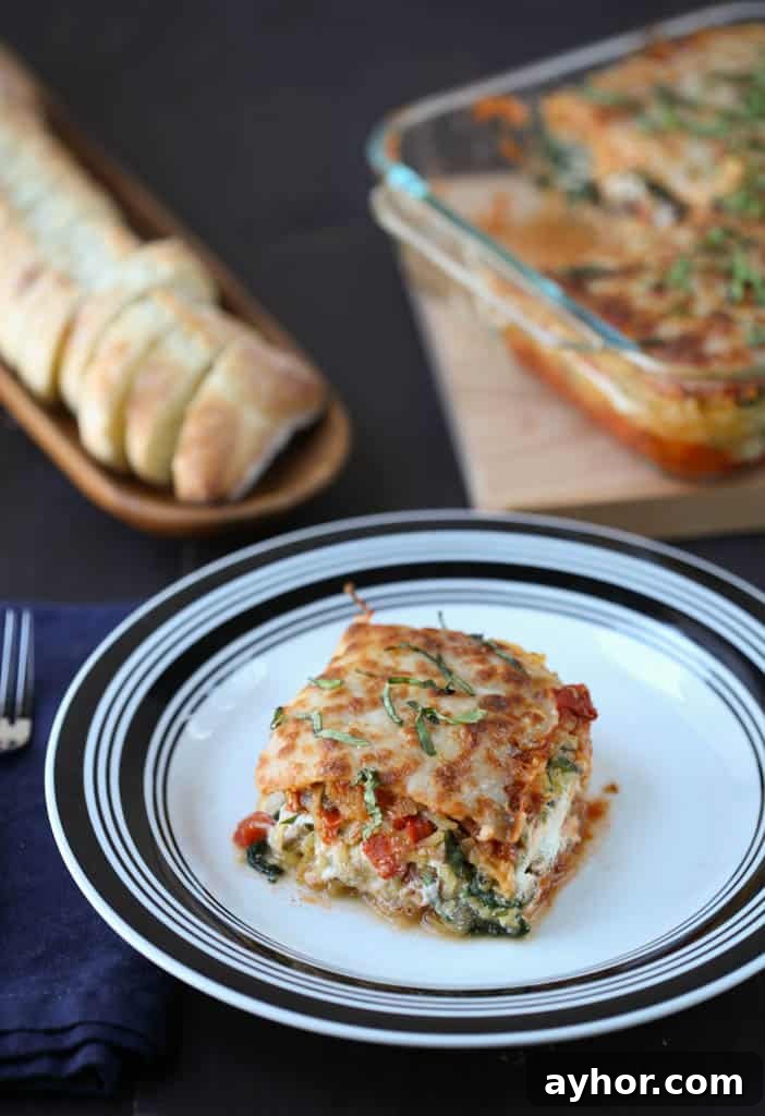 Spaghetti Squash Lasagna Recipe: Low-Carb Cheesy Layered Bake 2 piece of spaghetti squash lasagna on a black and white plate with a whole lasagna and sliced bread in the background.