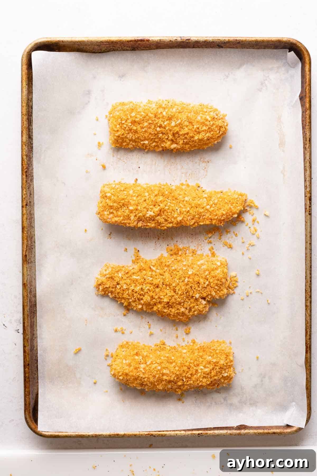 Crispy Panko-Crusted Cod with Lemon Herb Sauce 4 uncooked cod pieces crusted with panko on baking sheet.