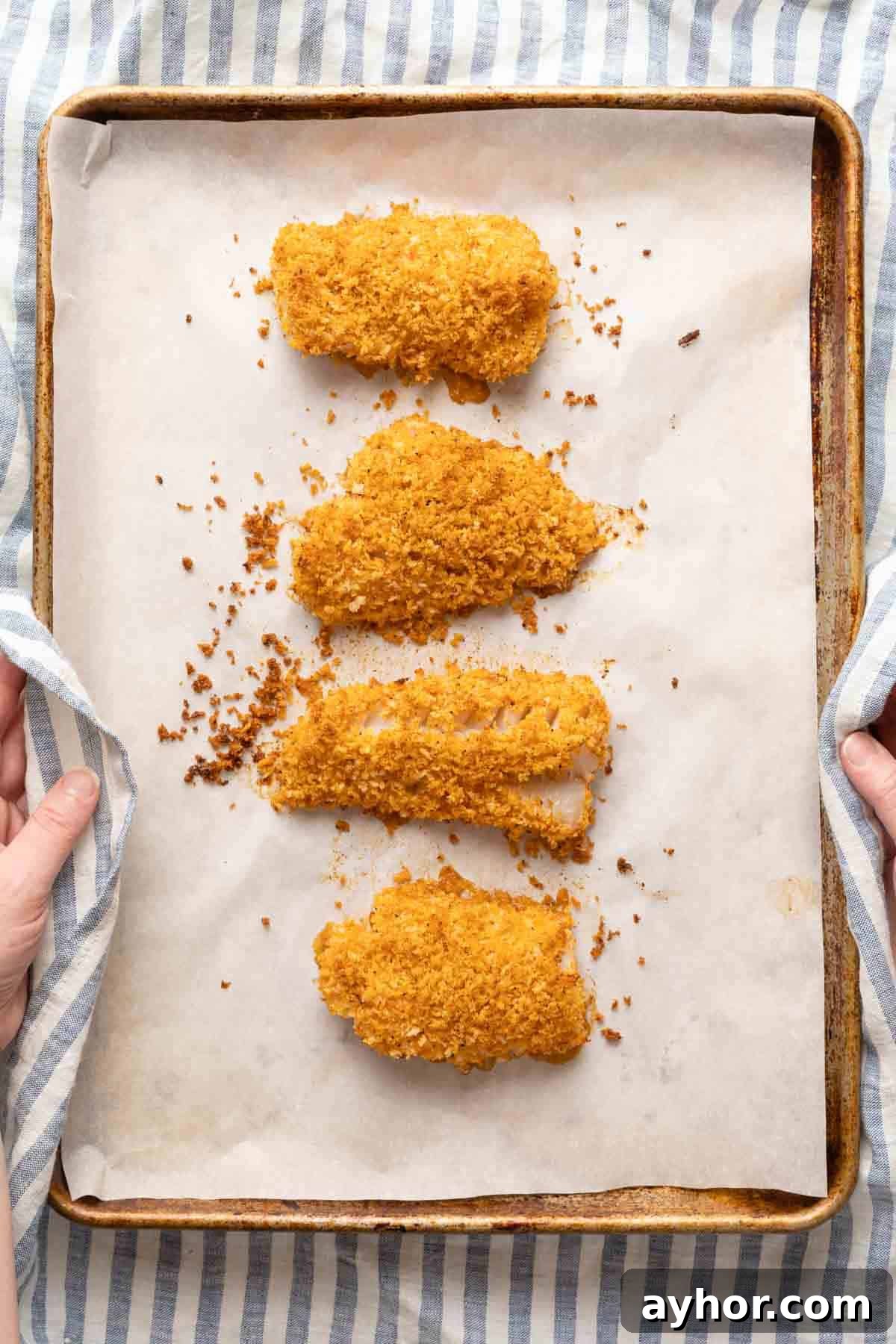 Crispy Panko-Crusted Cod with Lemon Herb Sauce 5 hand holding baking tray with baked panko crusted cod.