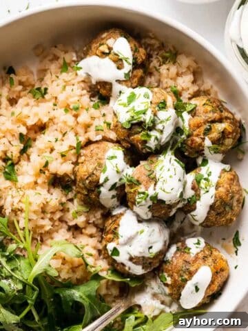 turkey meatballs in bowl with greens and yogurt sauce on top
