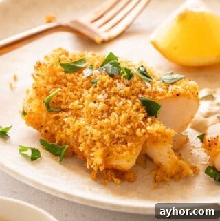 cod fillet crusted with panko crumbs on plate with fork and lemon on the side.