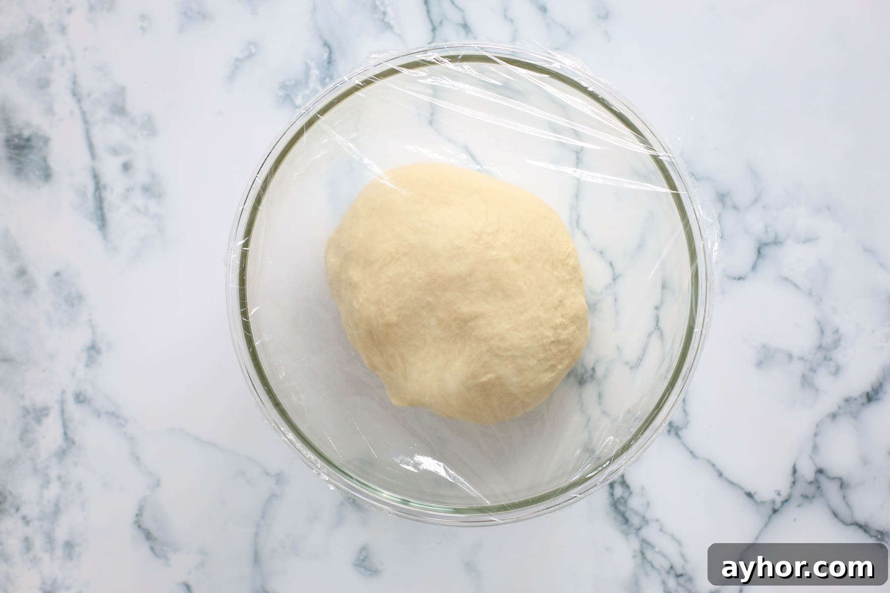 Dough covered with plastic wrap inside glass bowl.