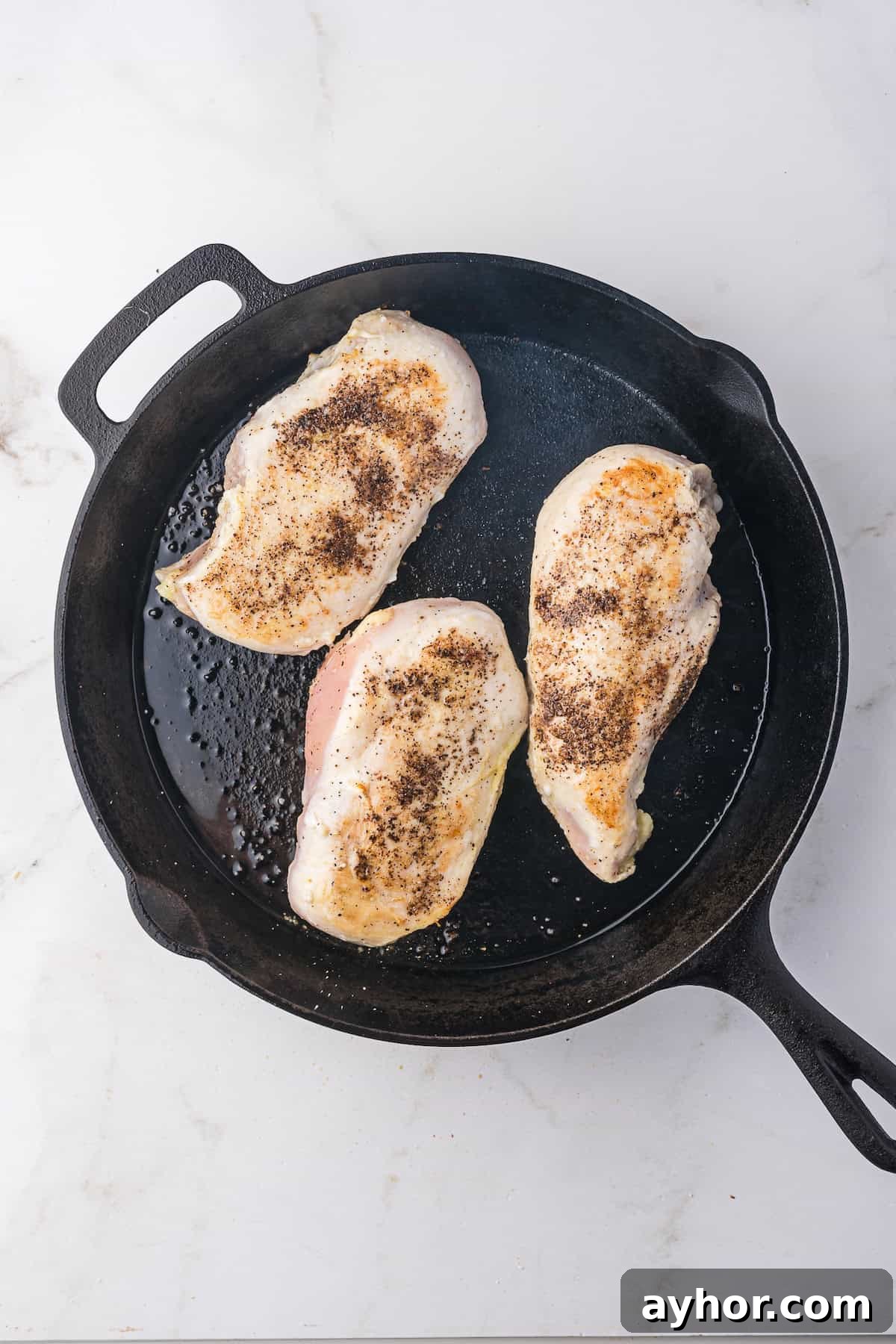 Three seasoned Lemonade Chicken breasts sizzling in a cast iron skillet.