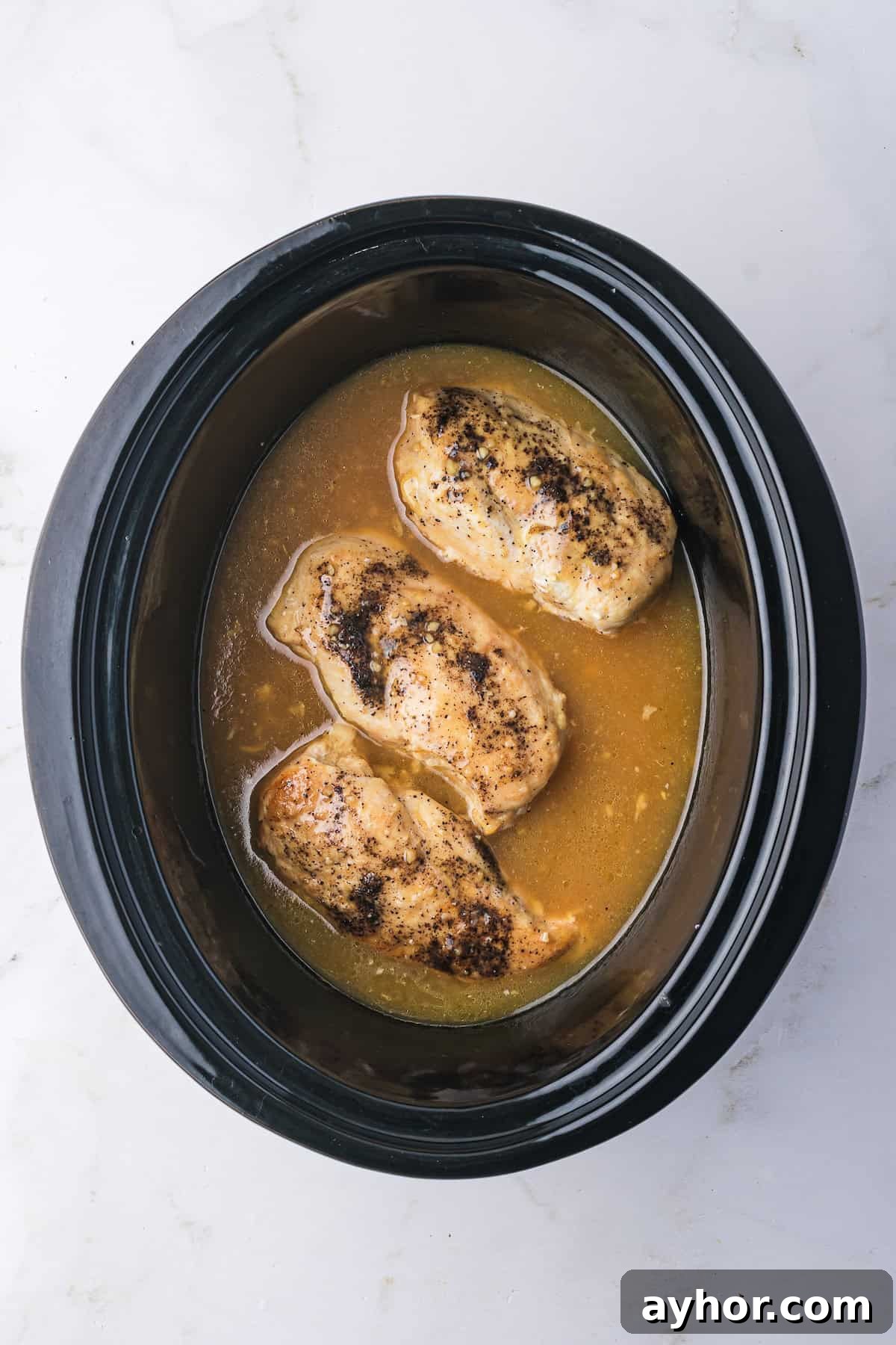 Chicken breasts simmering in a slow cooker with lemonade sauce.