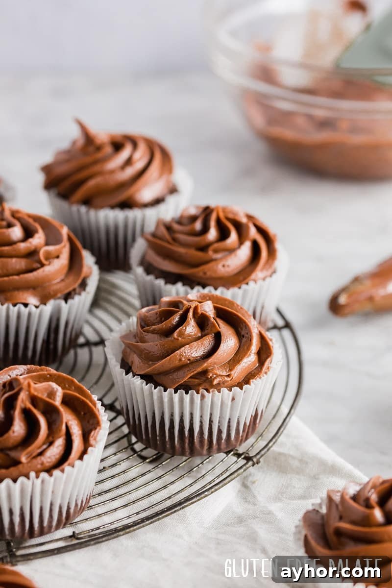 chocolate cupcakes in white paper liners topped with chocolate frosting, on a wire cooling rack