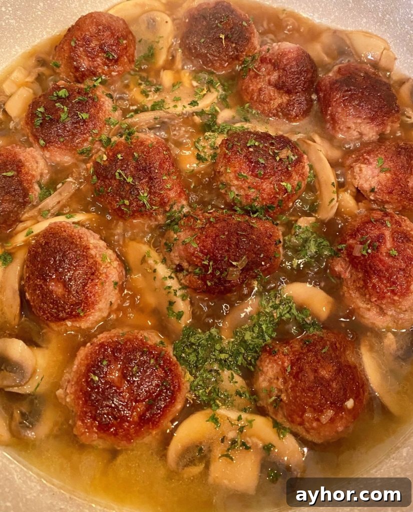 Meatballs and broth simmering in large pan.