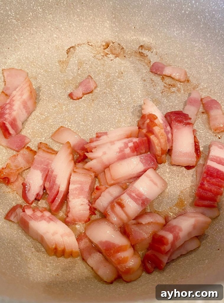 Bite size piece of bacon browning in a skillet.