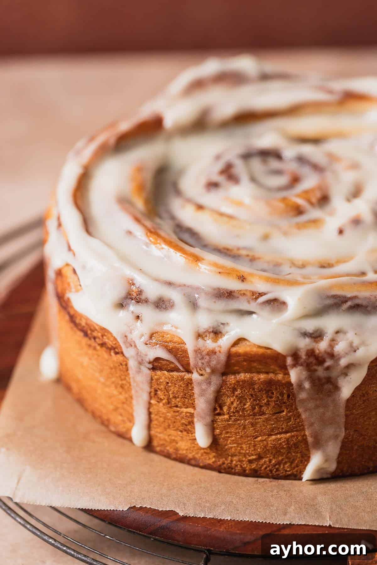 Cinnabon-Style Cinnamon Roll Cake Recipe 13 Cinnamon bun cake topped with cream cheese icing on a wooden serving platter.