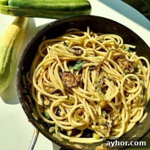 A pan of spaghetti with sliced zucchini and herbs