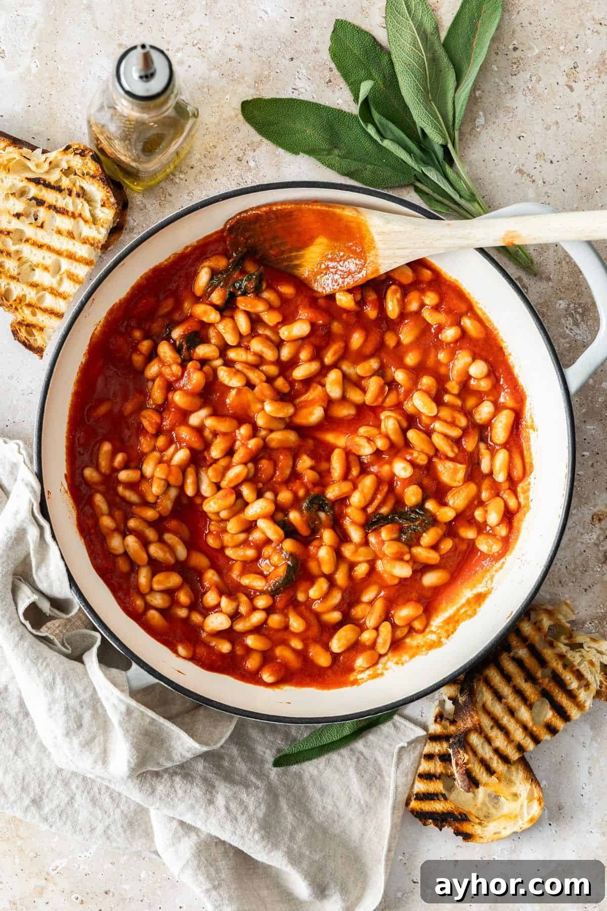White saucepan with Tuscan Stewed Beans, with a wooden spoon resting in the pot, ready for serving.