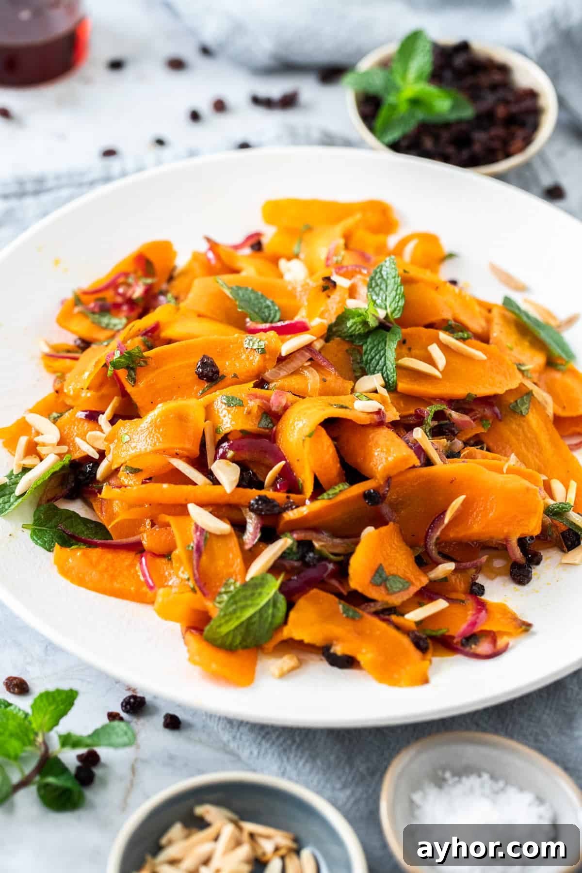 Round white dish of carrot salad, garnished with slivered almonds and mint leaves.