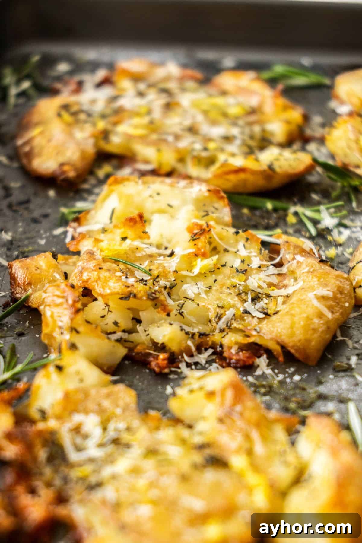 Roasted Smashed Potatoes, garnished with rosemary, grated Parmesan and lemon zest on a sheetpan.
