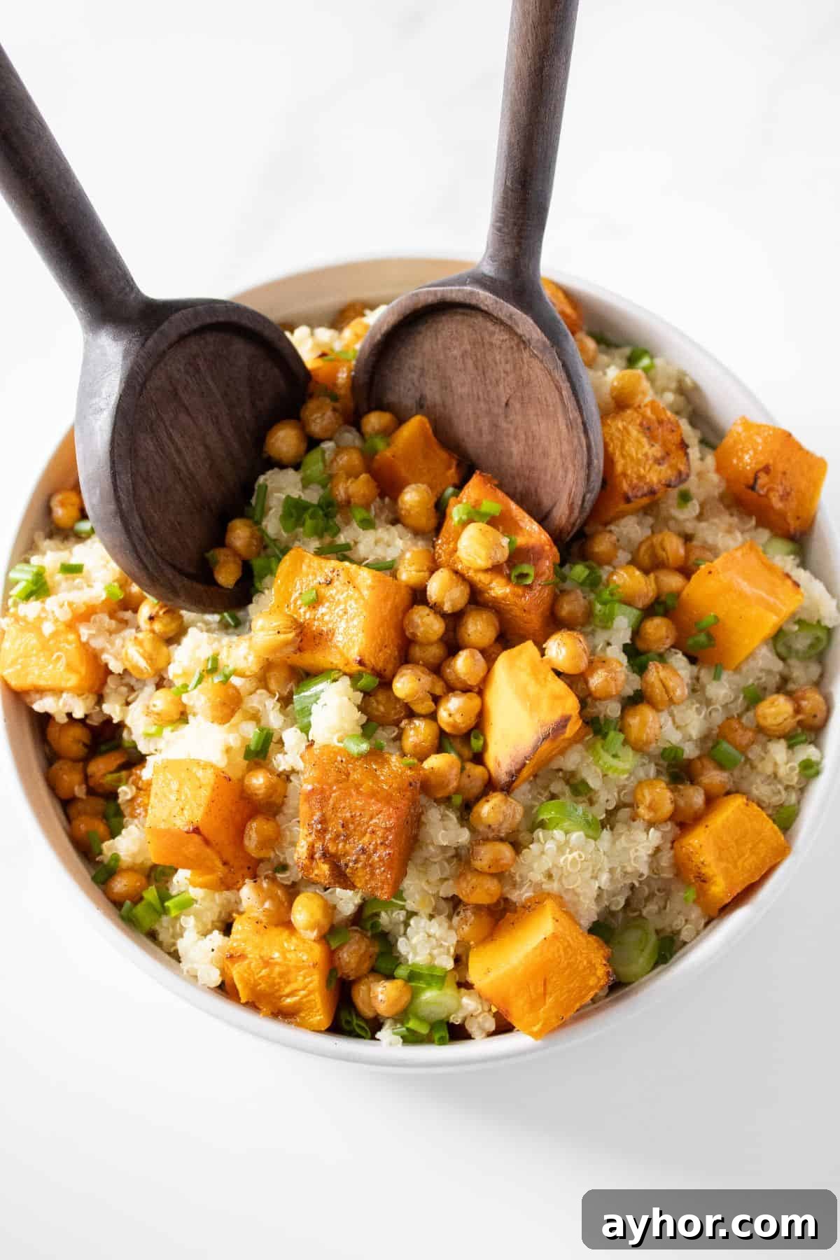 Round bowl of Pumpkin and Quinoa Salad topped with spring onions and chives, with wooden salad servers lifting some up.