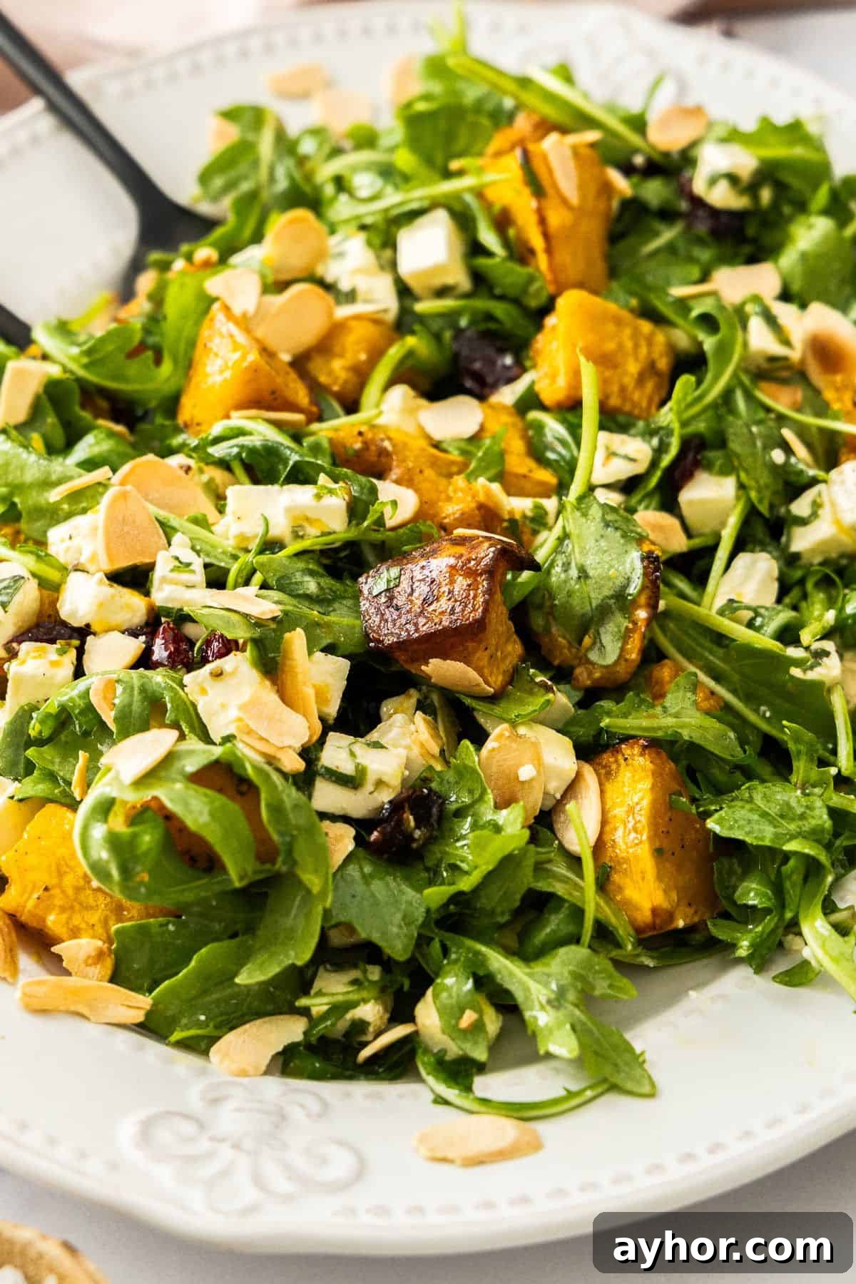 White oval platter of Roast Pumpkin and Feta Salad, with black salad servers resting in the dish and a pink cloth on the side.